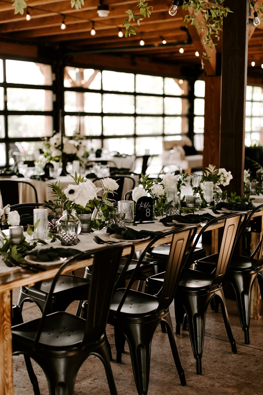 Floral arrangements lining a long table set with a palette of greens, blacks, and whites.