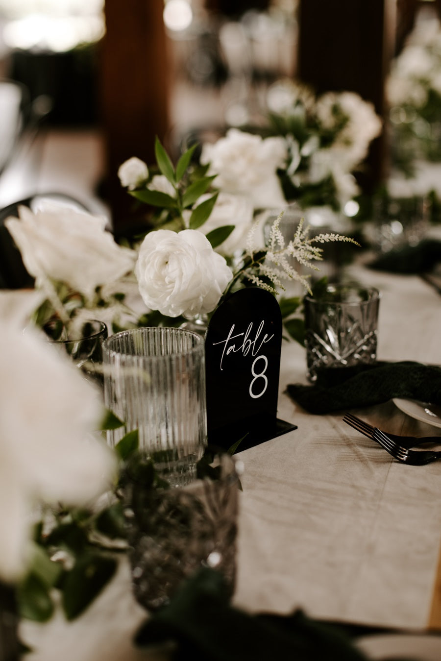 Close up of a floral arrangement centerpiece w/ votive candles and a black table number 8.