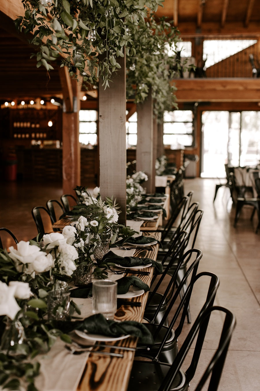 Table setting shot showing the low floral centerpieces and the centerpiece with greenery on a pedestal above the table.