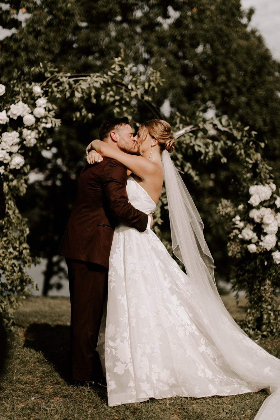 Bride and Groom embrace in front of the white and green floral archway