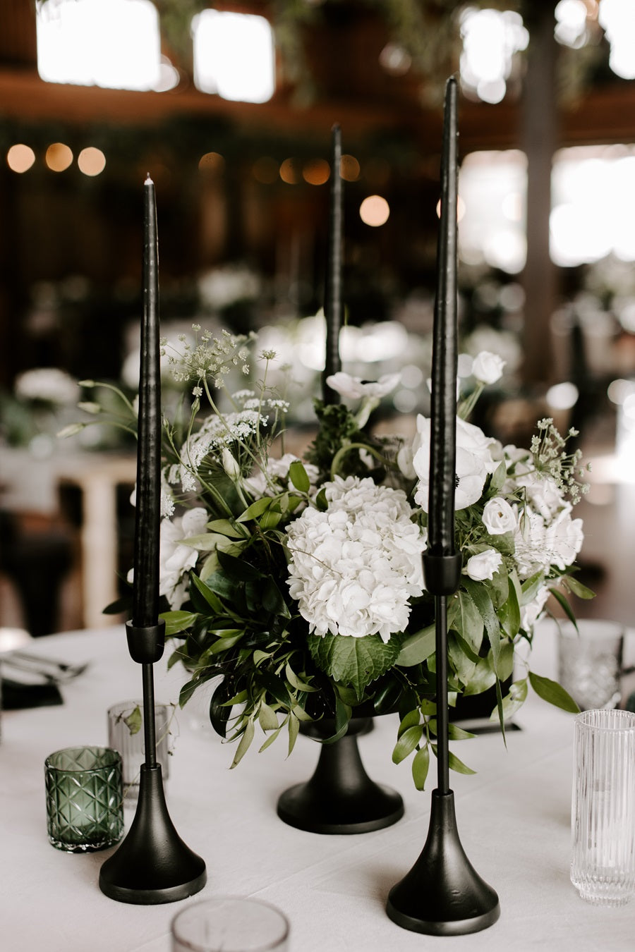 Close up on a floral centerpiece with white/green/black, accented with black taper candles and green/transparent votive candles.