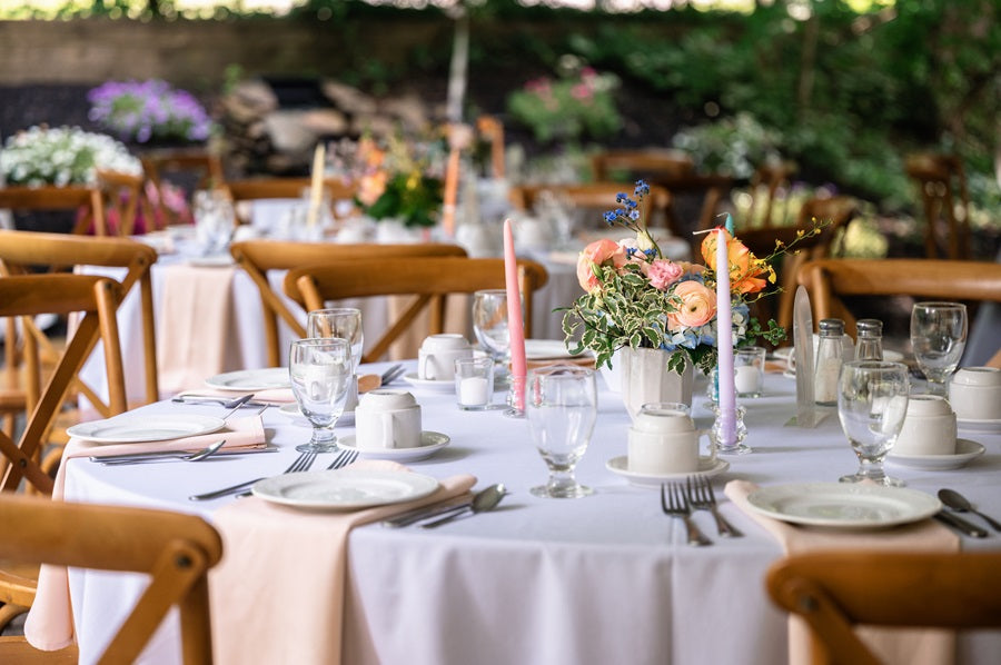 A wide shot showing round tables with colorful centerpieces and table candles. Table setting is neutral with light pink napkins.