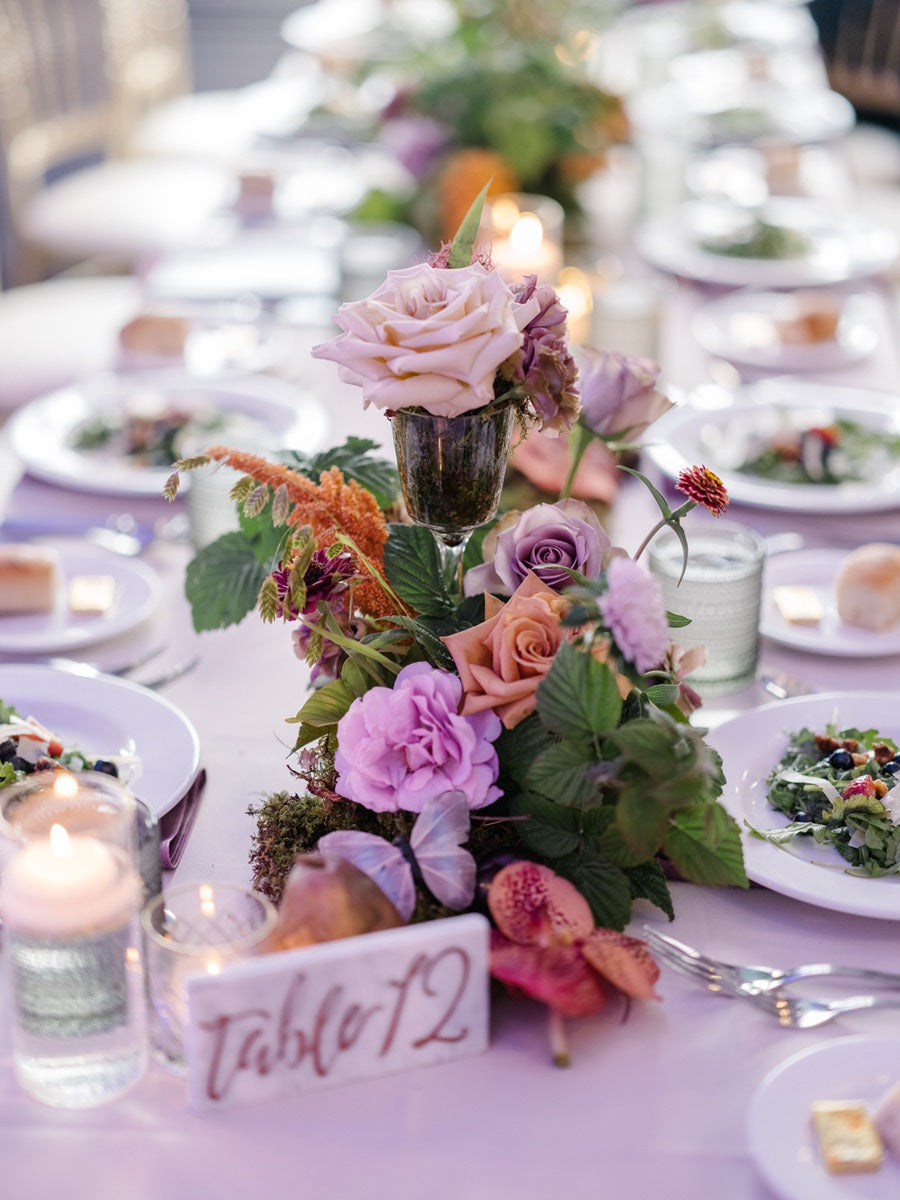 Floral centerpieces down the table center. The centerpieces are pink, orange, purple, and green.
