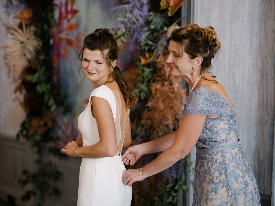 Getting ready shot of the bride and her mother. Background is floral, greenery and butterflies in a blue, green, and purple color palette.