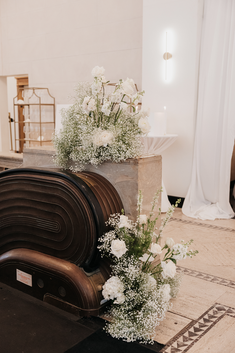 Soft green and white floral arrangements with babies breath and roses. Placed next to escalator stairs.