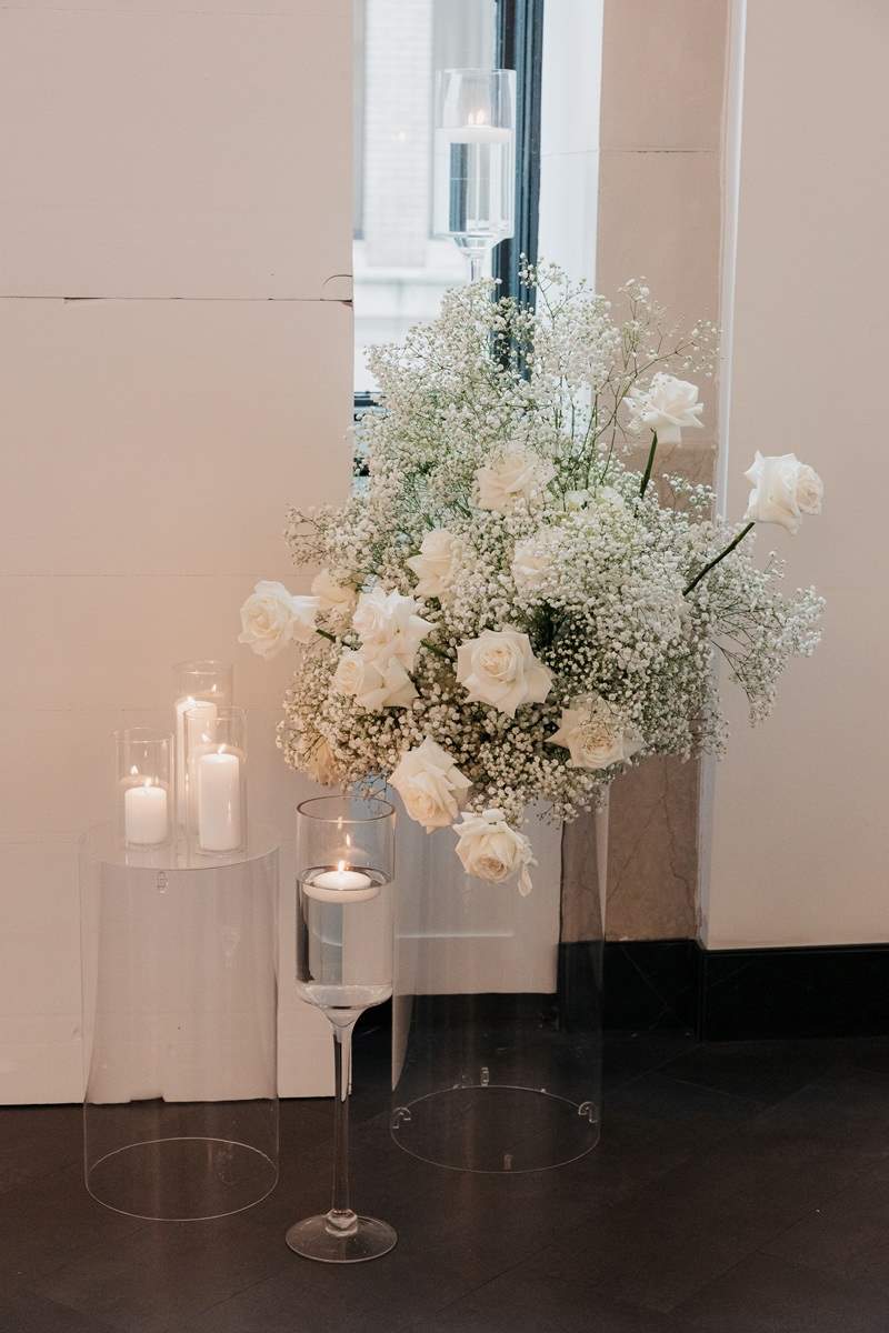 Close up on a green and white floral arrangement featuring roses and babies breath. Candles are placed arround the arrangement.