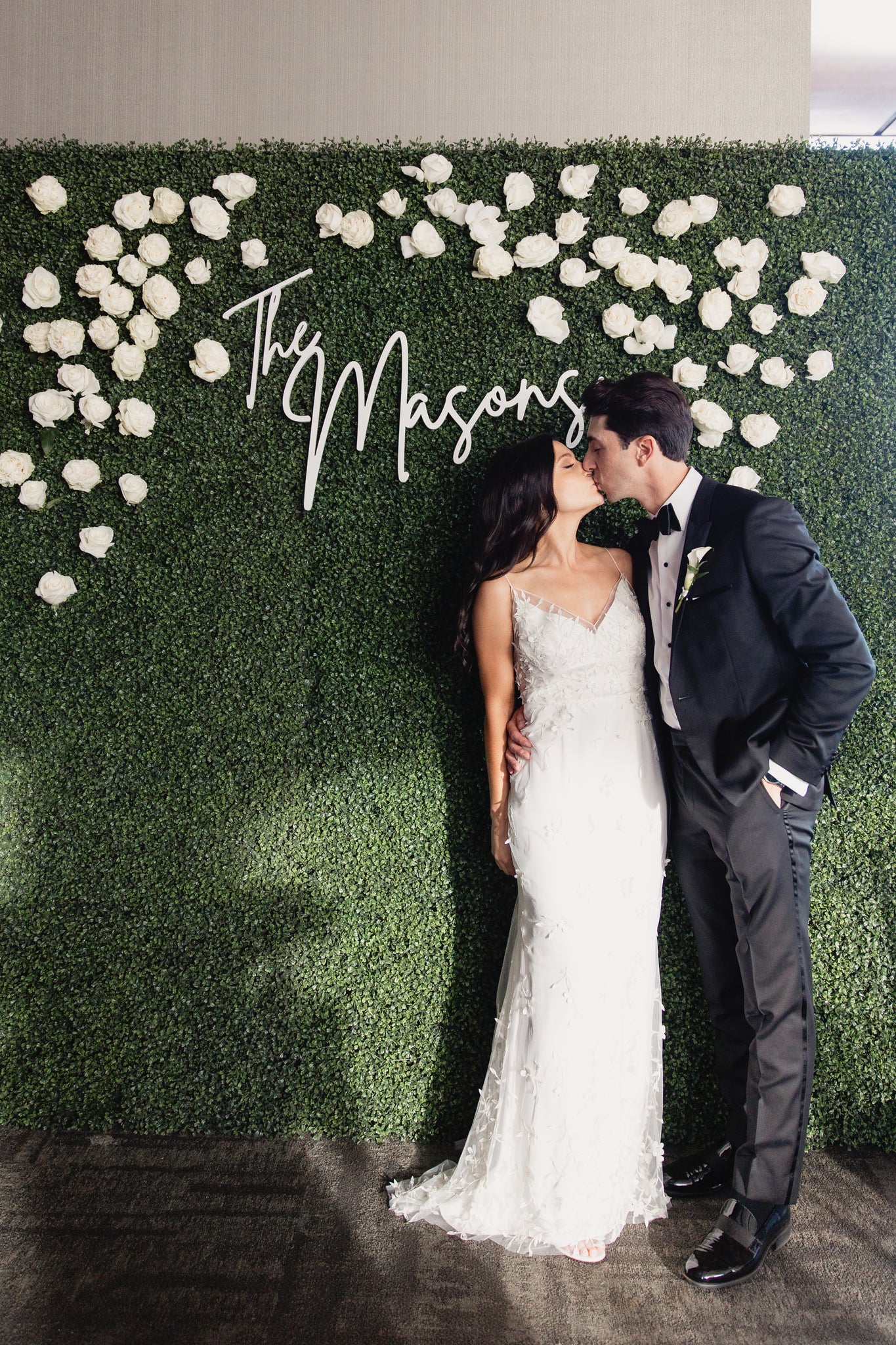 bride and groom kissing in front of boxwood wall 