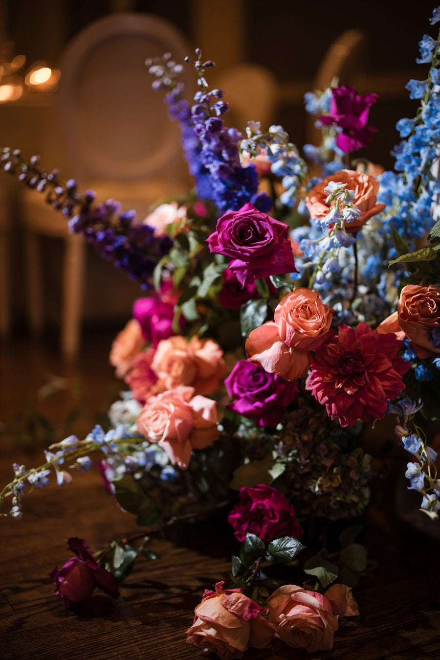 Close up on a floor floral arrangement. The colors are blue, peach, pink, purple, and green. Flowers pictured are roses, hydrangea, orchids, delphinium, and assoreted greenery.