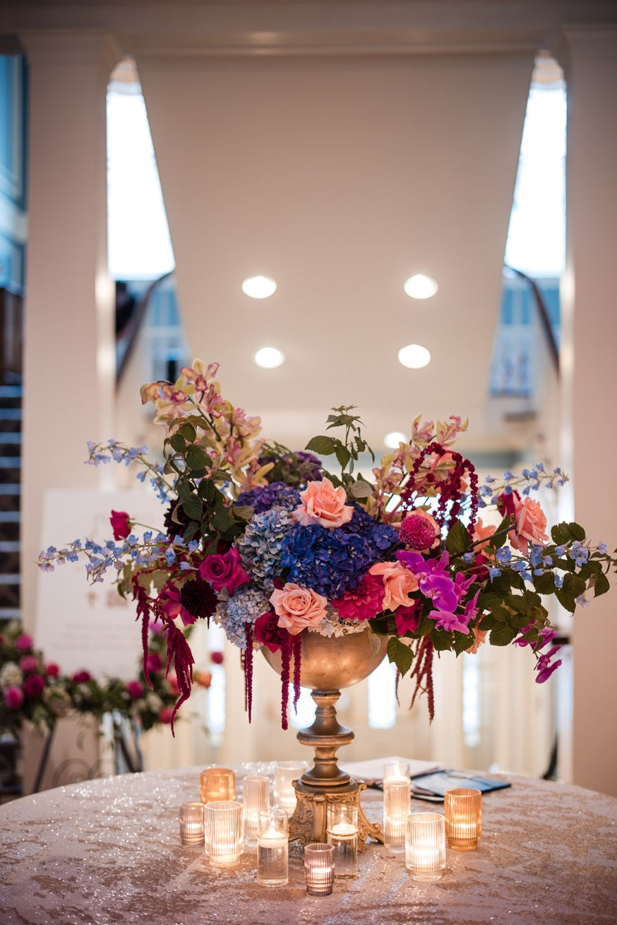 A large floral arrangement at the entrance to the reception. Florals are pink, purple, peach, blue, and green. Some florals pictured are roses, hydrangea, orchids, and delphinium.