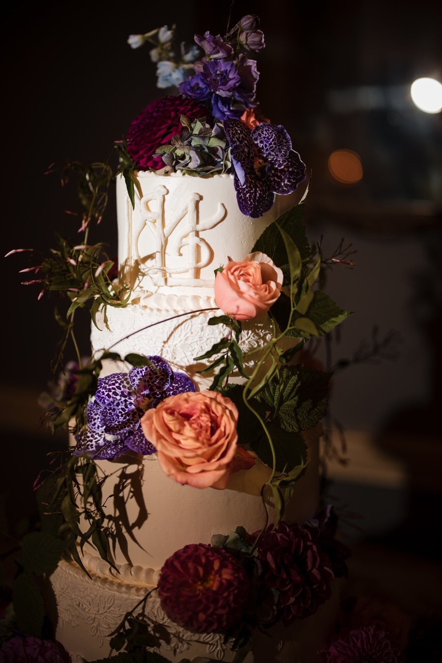The cake is white with floral texture and fresh floral/greenery climbing up the sides.