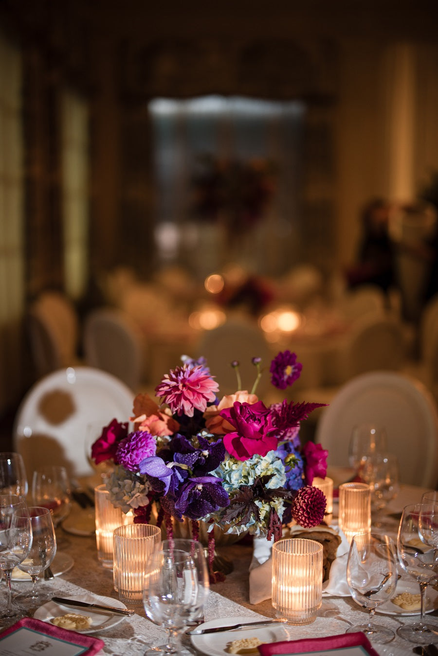 A jewel toned centerpiece on a round table. The tableware is neutral with matching pink napkins.