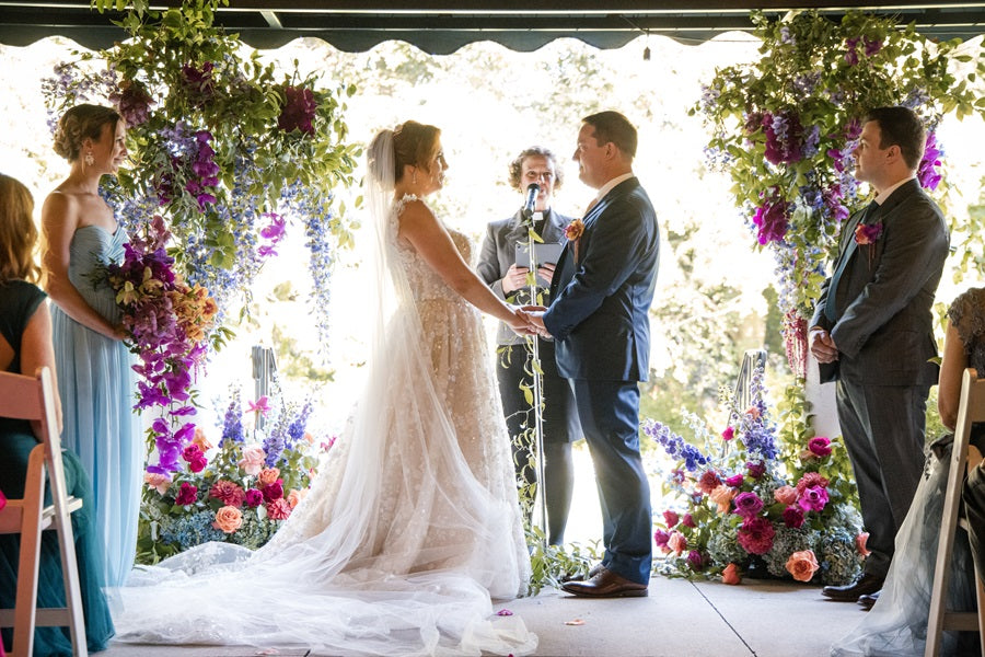 Photo of the bride and groom at the "altar", lush florals on either side of them.
