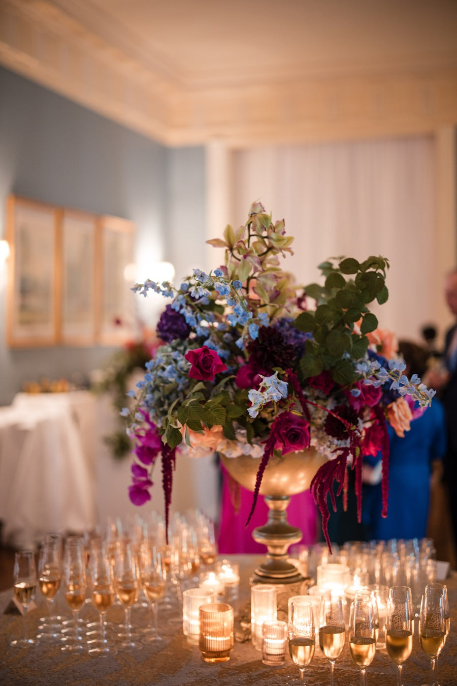 A floral arrangement with jeweltoned colors in a gold compote. Placed on a table with the cocktail hour champagne.