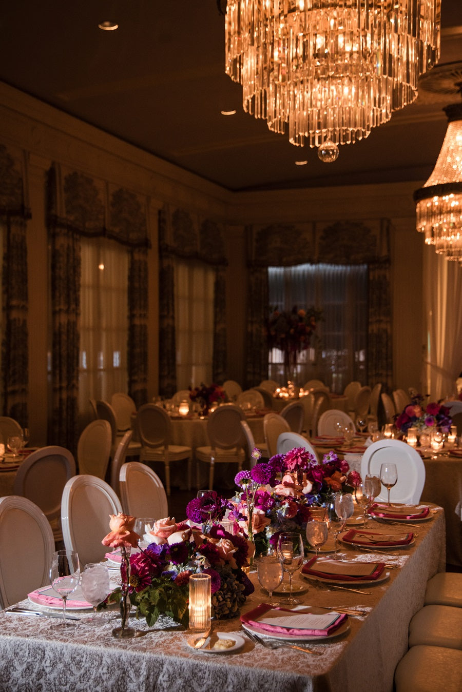 A wide room shot showing the jeweltoned centerpieces, candles, and tableware.