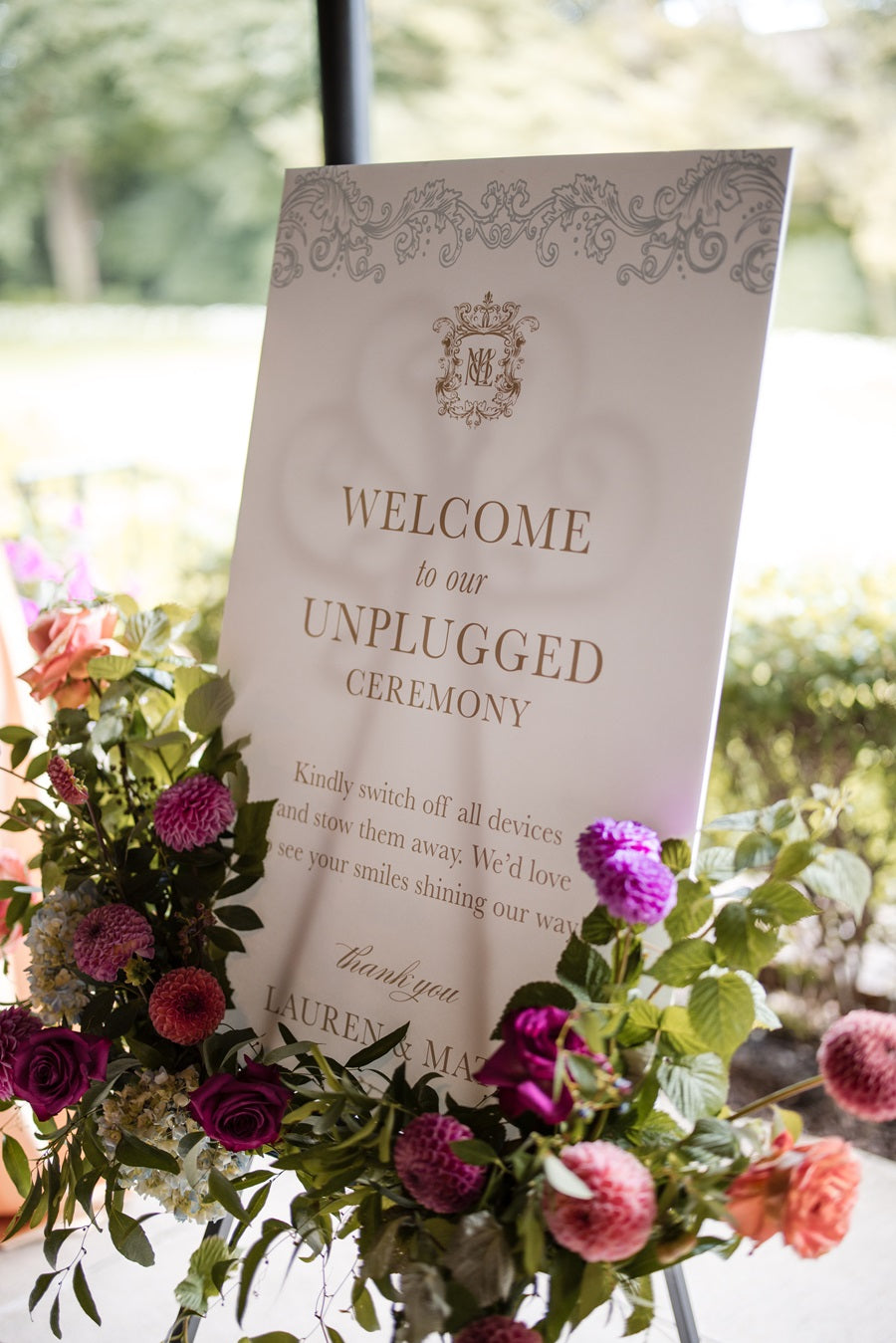 A white welcome poster with jewel toned florals lining the base of the sign.
