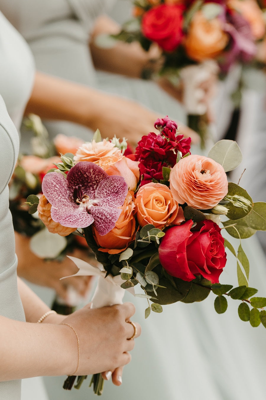 Close up on a bridesmaid's bouquet. Highlighting the colorful palette with orchids, roses, eucalyptus, and additional accent florals.