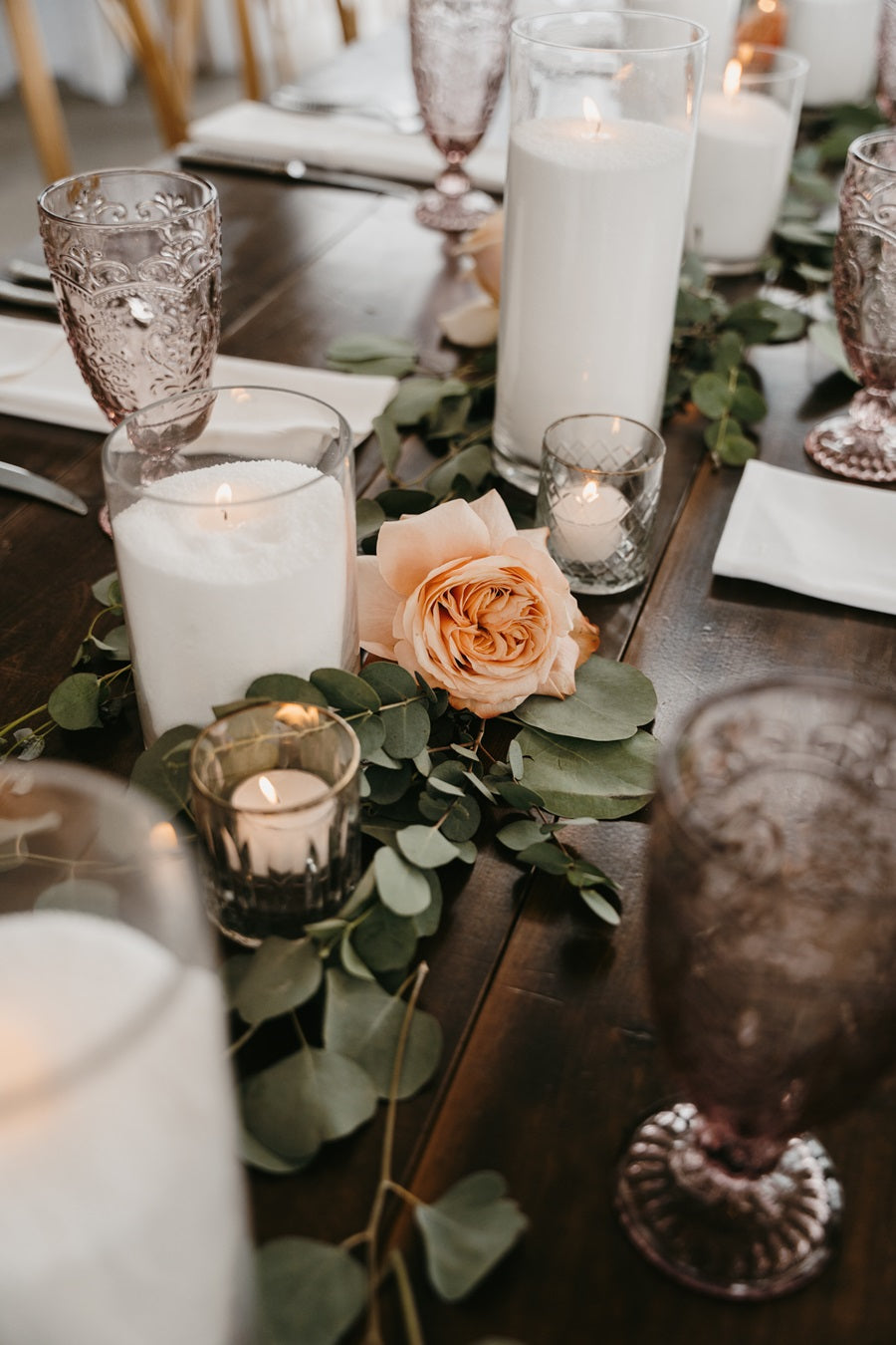 Close up on the guest table florals/greenery. Loose greenery and florals line the table, accented with tall candles and votives.