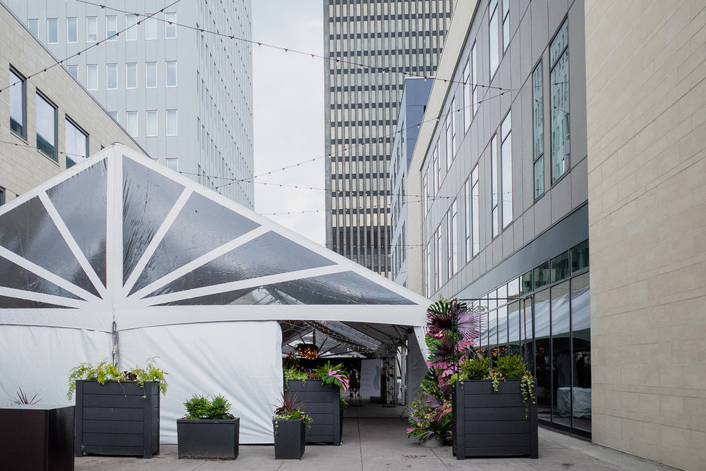 outside of tent with large planters of greenery