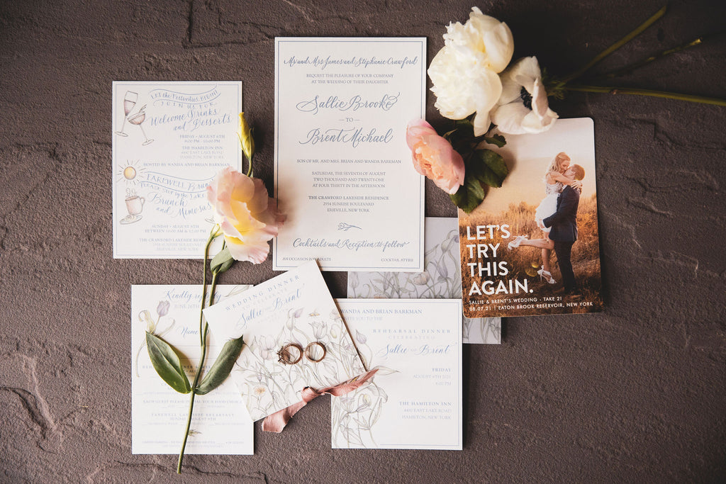 flatlay of wedding invite, wedding rings and loose blooms