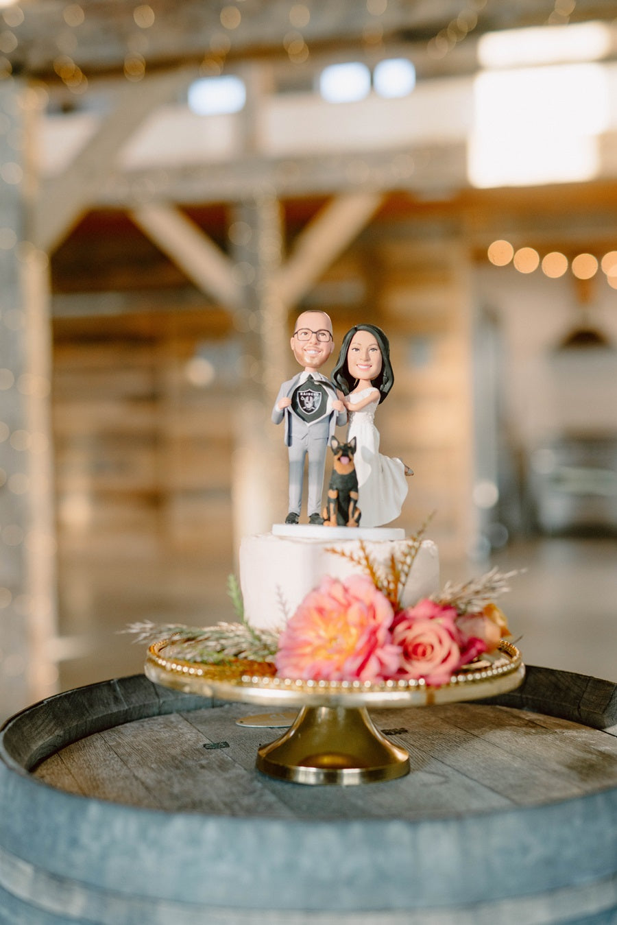 Bride and groom cake topper decorated with pink/peach roses, and greenery