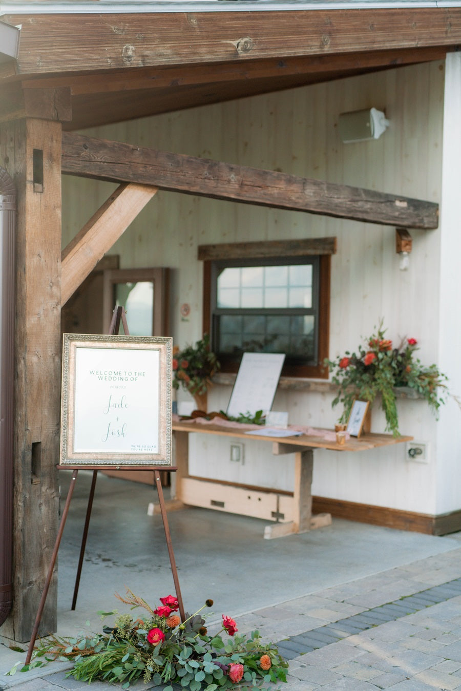 Welcome sign on an easel with florals at the base. Flowers on a shelf in the background as well.