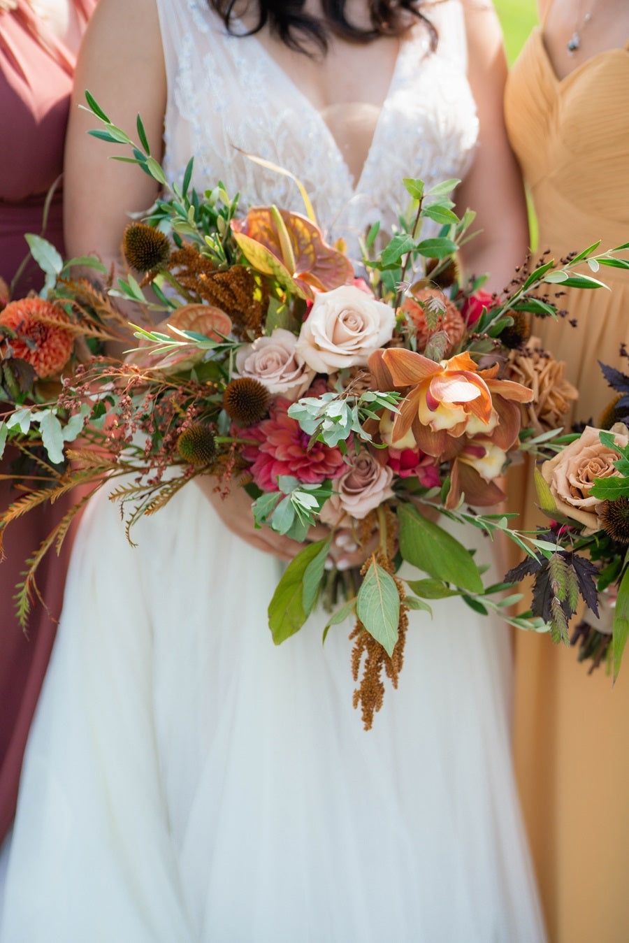 Close up on the bride's bouquet, featuring fall colors, roses, orchids, greenery, dahlias, and more.