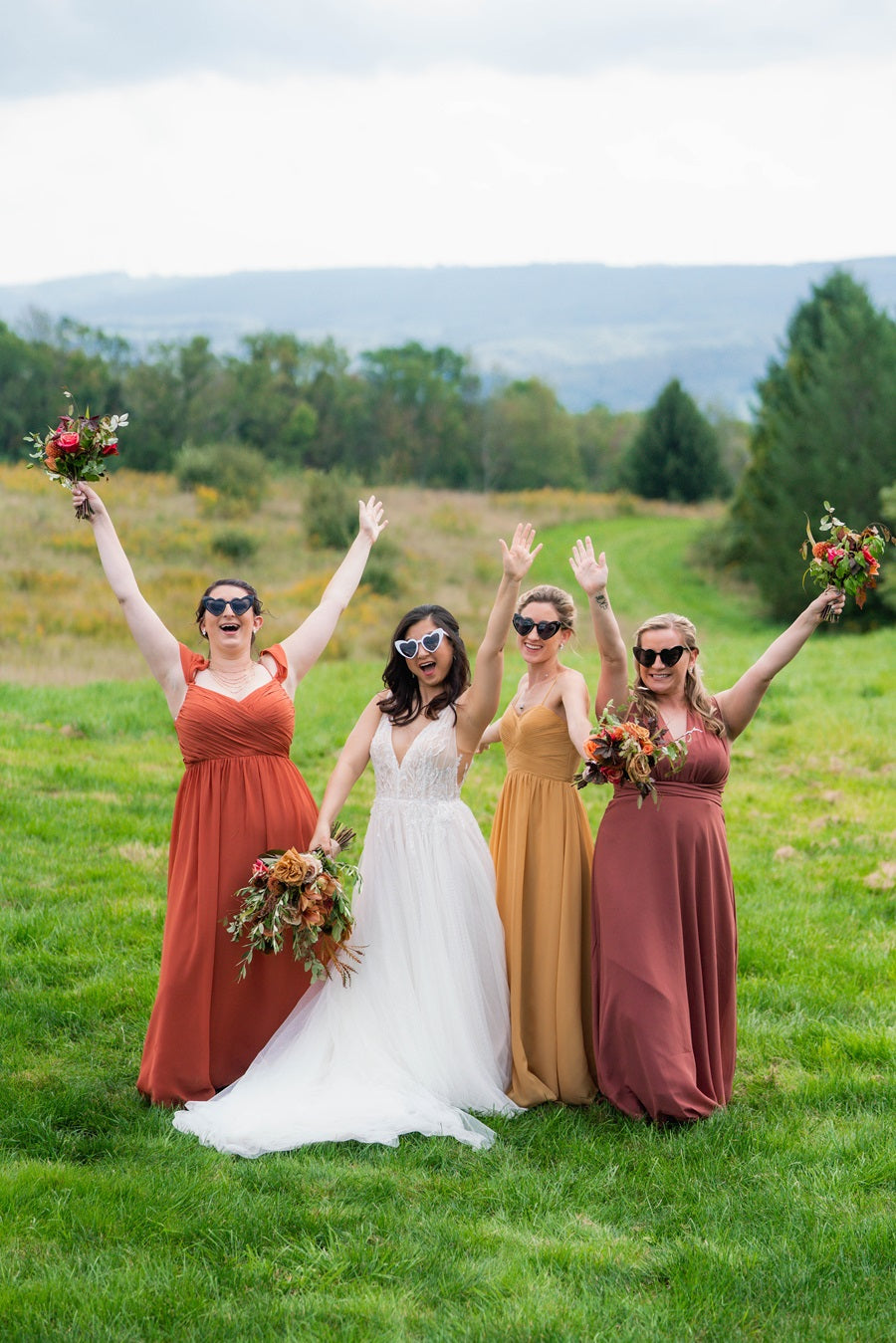 Bridal party wearing heart glasses, wearing a fall color palette, raising their arms in the air.