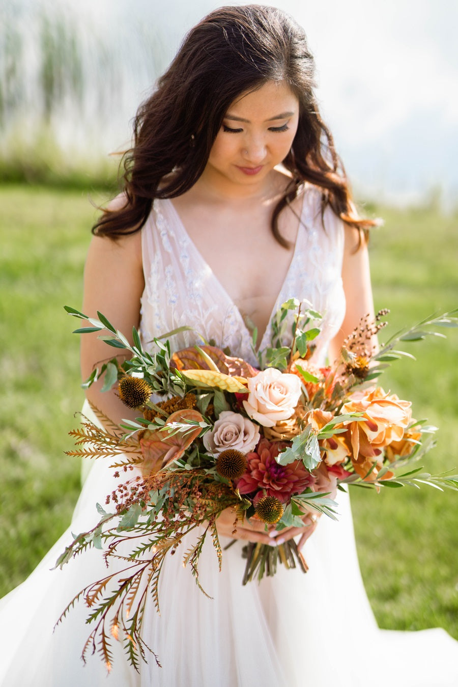 Bride holding bridal bouquet, fall colors, aesymmetric style, roses, dahlias, and orchids.