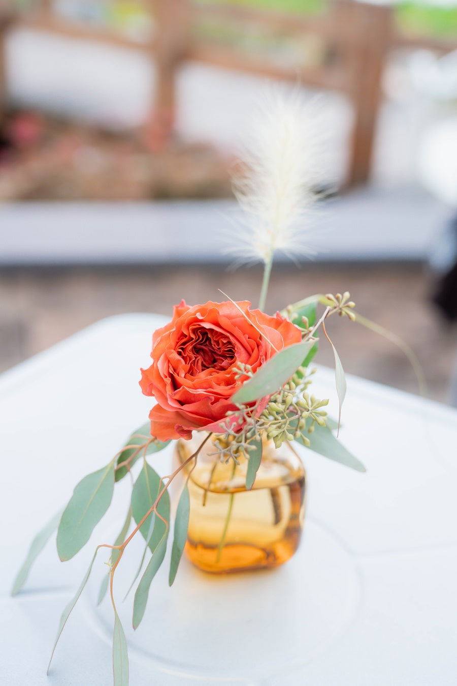 Cocktail table arrangement in a small yellow tinted budvase, with a garden rose and accent greenery.