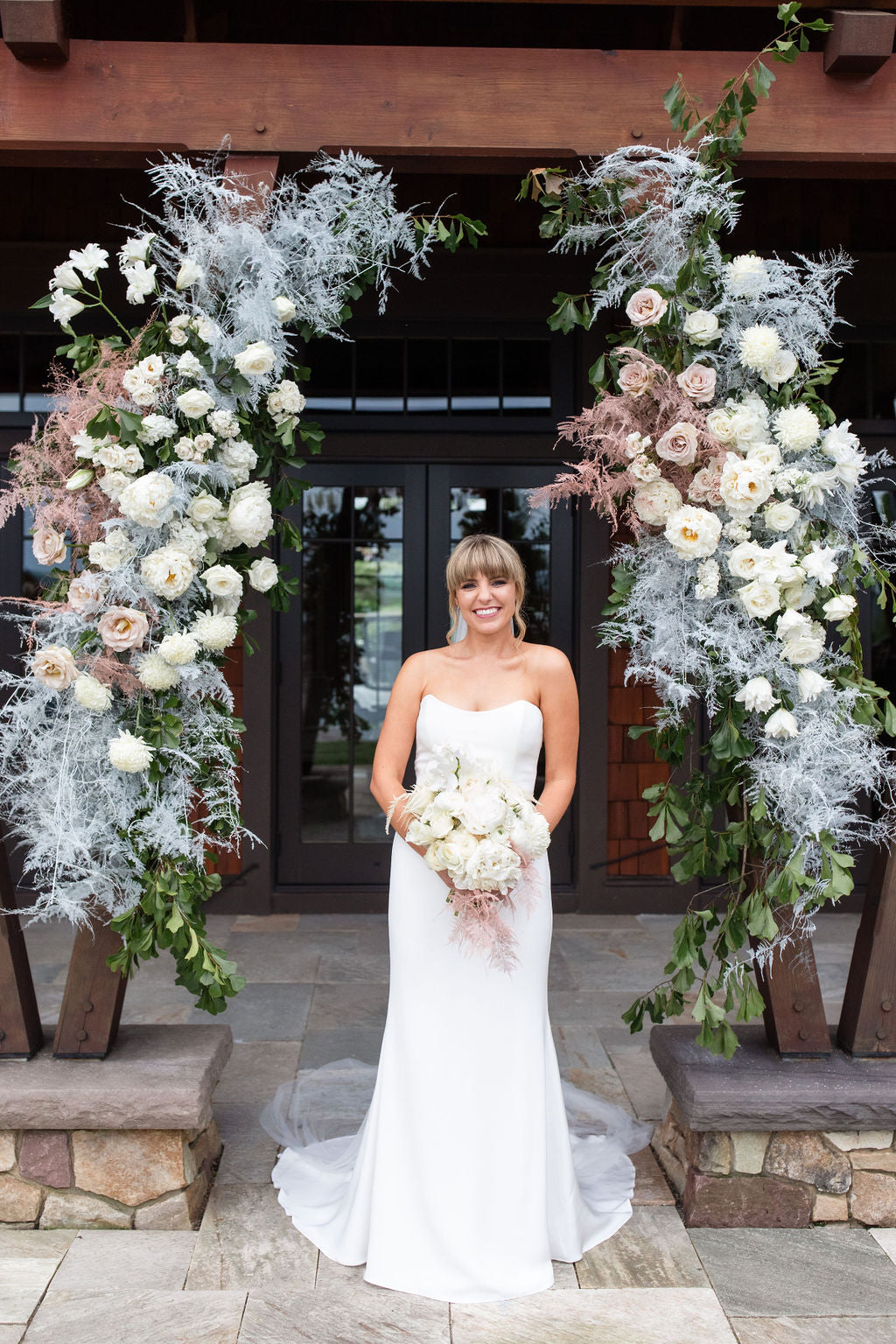 Bride in front of floral arch holding white bridal bouquet