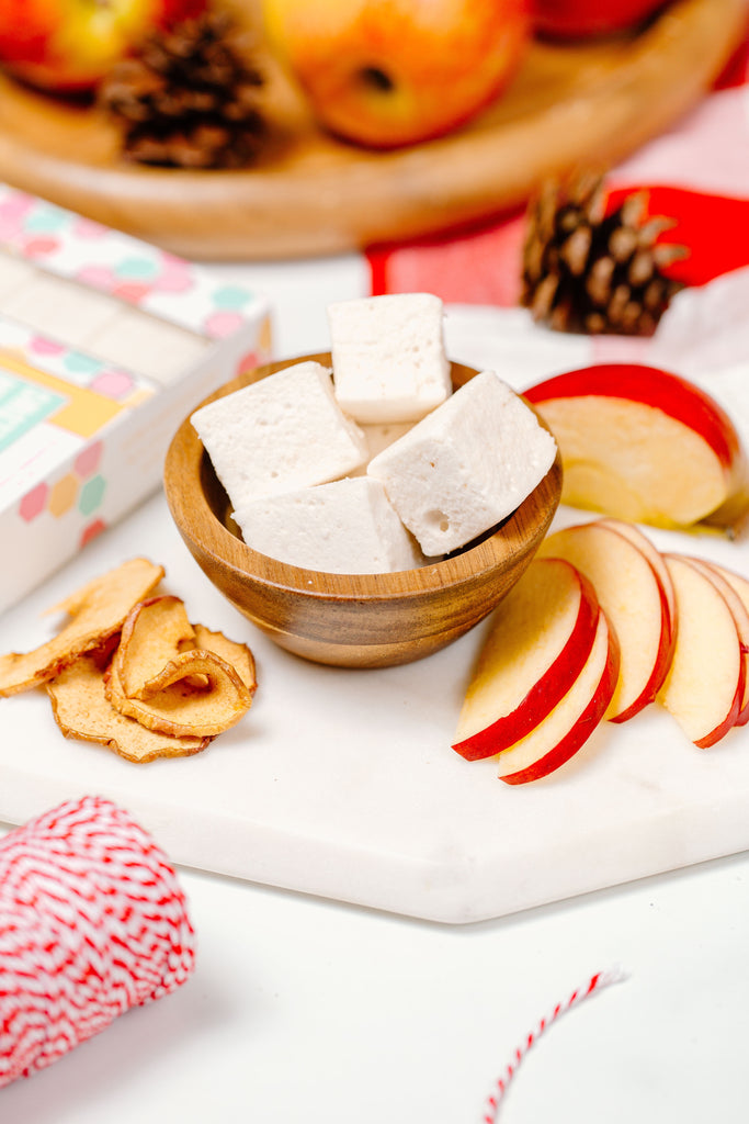 Apple Cinnamon marshmallows in a bowl next to apple slices and cinnamon sticks