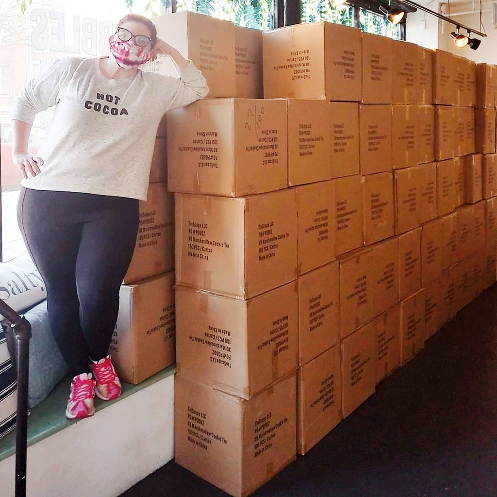 Kat Connor, co founder of XO Marshmallow, stands in front of 10,000 hot cocoa tins