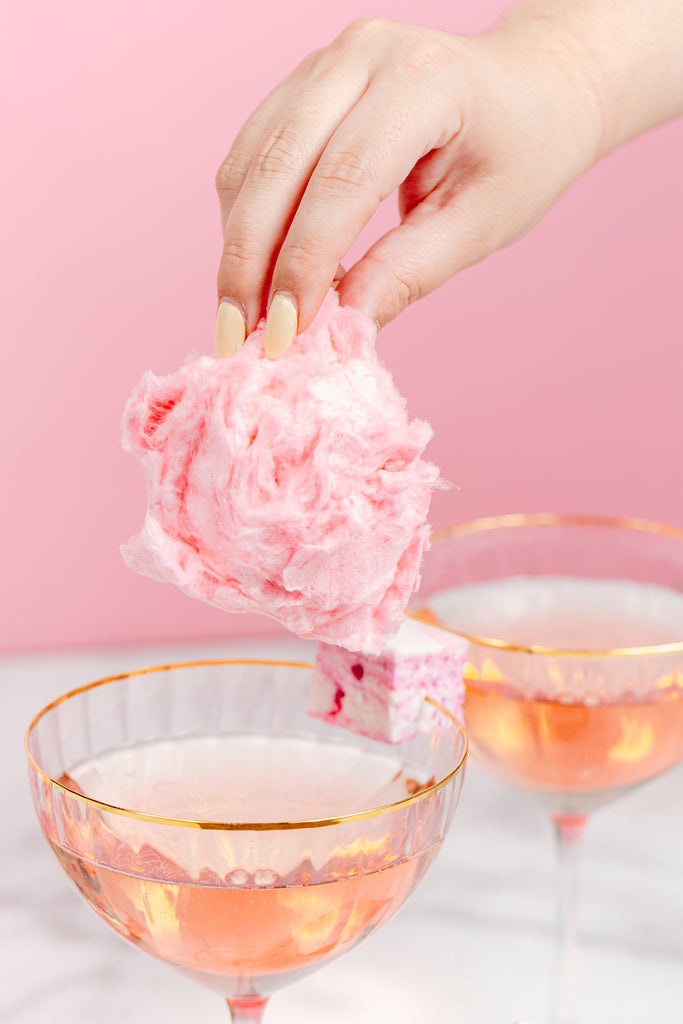 A hand hovers a ball of cotton candy over a glass of rosè, getting ready to add the final touch to the xo marshmallow cocktail