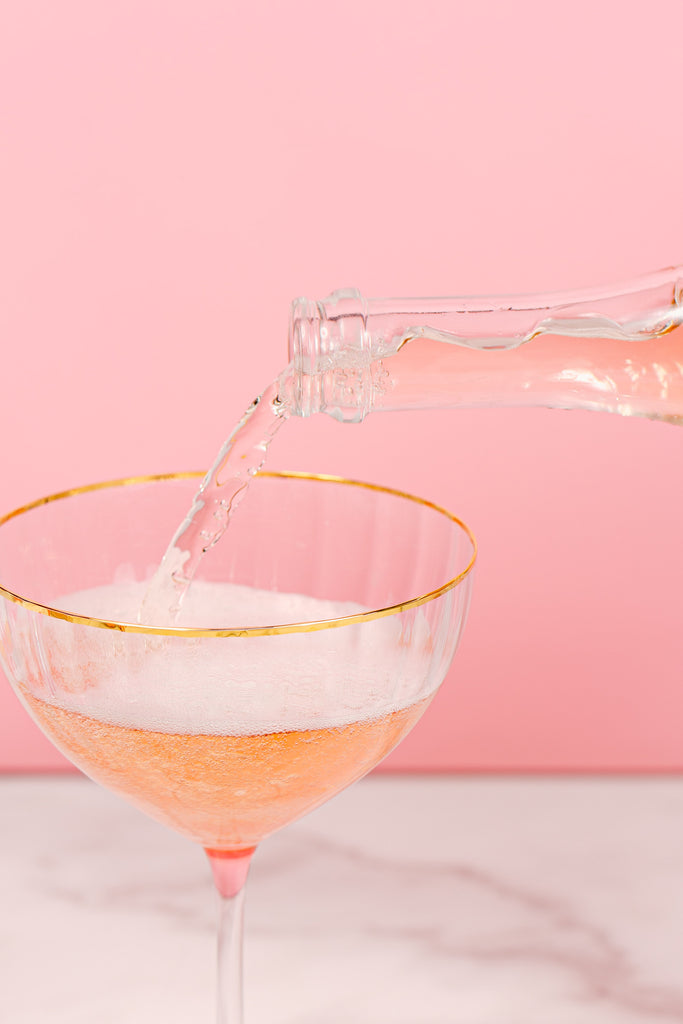 Pouring rosè into a gold rimmed champagne coupe 