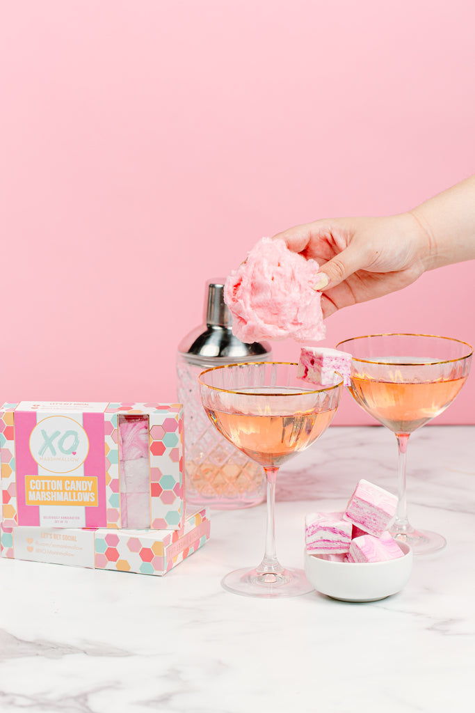 A hand adding cotton candy to the top of champagne and adding a garnish of cotton candy marshmallows  
