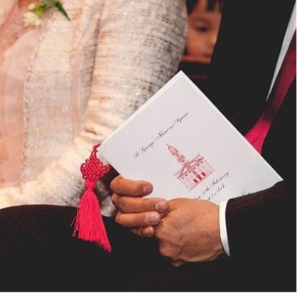 A picture of a wedding guest holding an order of service with an image on the cover and tassel inside