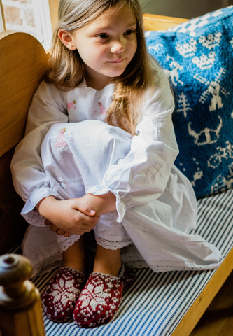Little girl wearing red slippers with knitted Norwegian Selbu star motif.
