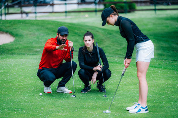 A golf coach checks how well a student hits the ball