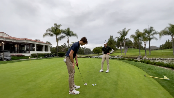 A golf student reeling in his shot while taking note of the wind by his coach 