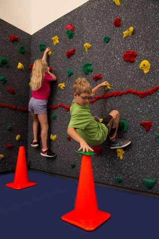 Boy moving a bean bag from a climbing wall to a cone in a fun Traverse Wall activity called Cone Challenge