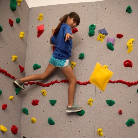 Girl tossing a bean bag at a target while rock climbing