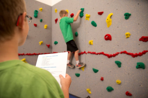 Boy rock climbing while his partner gives him suggestions