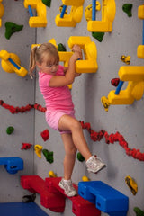 Girl rock climbing using grab-bar style hand holds and ledge-style foot holds