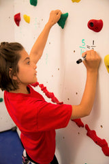 Girl rock climbing and writing on a dry erase climbing wall