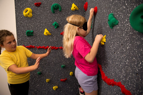 Girl rock climbing while blind folded while partner leads her verbally