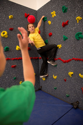 Boy tossing ball to girl on a climbing wall by Everlast Climbing