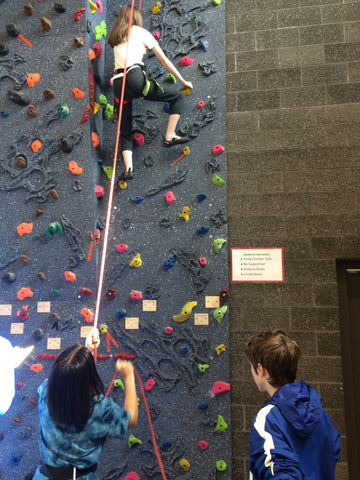 Student belaying another student who is climbing up the climbing wall