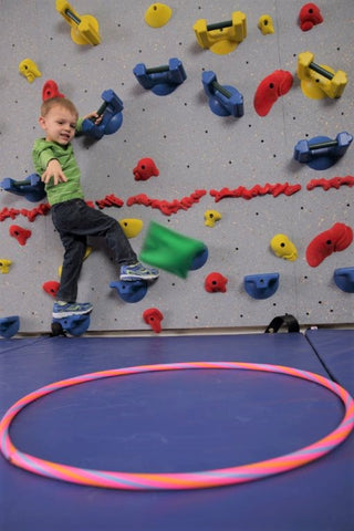 Small boy rock climbing while tossing a bean bag into a hula hoop target on the safety mat