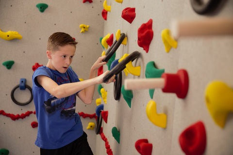 Boy rock climbing using ultimate challenge course hand holds