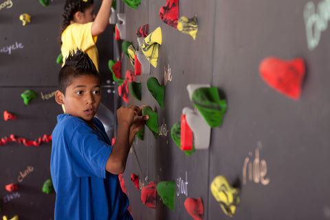 boy rock climbing using only holds labeled with verbs to practice parts of speech
